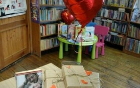Na biurku są wyłożone książki zapakowane w papier i przystrojone serduszkami, przyczepiony jest czerwony balon i kartka z napisem : "Walentynkowa randka w ciemno z książką"