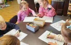 Przy stołach siedzą dzieci i robią karty pracy i kolorują zwierzątka. Z tyłu widać nauczyciela, kt&oacute;ry obserwuje pracę dzieci.