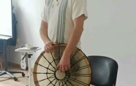 Szymon stoi przy krześle i trzyma jakis stary okrągły regionalny instrument.