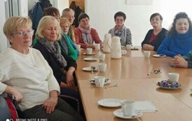 Przy stole z kawą siedzą emeryci i patrzą na występ Szymona.