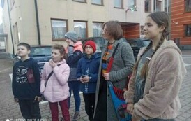 Młodzież stoi na placu przy Urzędzie Gminy i patrzy  w stronę busa..