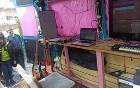 Widać wnętrz busa z monitorami, klawiszami i stoją dwie gitary elektryczne. Chłopcy tam zaglądają.