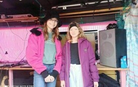 W busie nagraniowym stoją uśmiechnięte dwie dziewczyny. Po prawe stronie stoi głośnik.