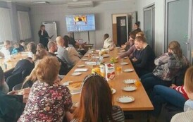 Przy stołach na białej sali siedzą licznie rodzice i ich dzieci oglądając na monitorze nagrania filmowe i muzyczne dzieci.