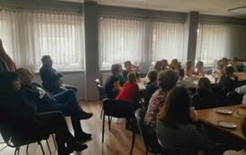 Przy stołach na białej sali siedzą licznie rodzice i ich dzieci oglądając nagrania filmowe i muzyczne dzieci.