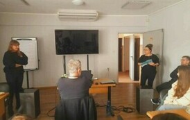 W białej sali w Goku jest spotkanie prowadzących warsztaty z dziećmi i ich rodzicami. Widać kierowniczkę biblioteki jak wita wszystkich.