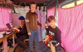 W busie obok Iwony jest dw&oacute;ch chłopak&oacute;w, jeden siedzi z gitarą elektryczną, a drugi obok stoi ze słuchawkami na uszach.