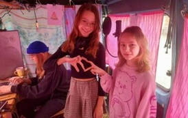 W busie przy komputerze siedzi Iwona Skwarek, a z przodu stoją dwie dziewczynki układając swoje palce w kształt serca.