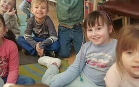 Na dywanie siedzą dzieci i słuchają bajki czytanej przez bibliotekarkę.