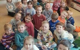 Dzieci siedzą w grupie na karimatach, z tyłu po środku siedzi bibliotekarka z książeczkami świątecznymi w ręku pokazując je.