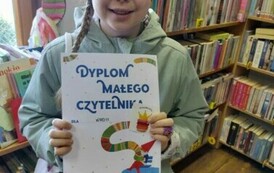 Dziewczynka w opasce na uszach pokazuje sw&oacute;j dyplom.