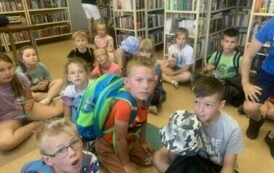 Grupa dzieci siedzi na podłodze w  bibliotece