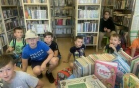 Dzieci siedzą na podłodze w bibliotece, obok stoi mały stolik z bajkami dla dzieci.