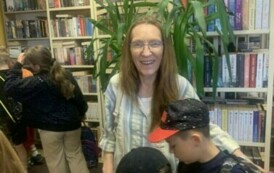 Bibliotekarka Gabriela stoi przy dzieciach i się uśmiecha.