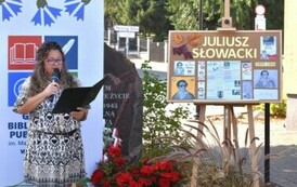 Po lewej stronie stoi kierowniczka biblioteki z mikrofonem i wita publiczność,a za Nią stoi rolka z logiem biblioteki. Po prawej stronie stoi  tablica korowa z informacjami o Juliuszu Słowackim.