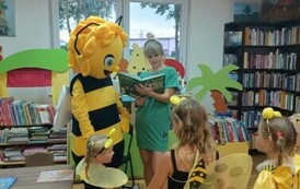 Pani bibliotekarka czyta bajkę, a dzieci przebrane za pszcz&oacute;łki stoją razem z dużą pszcz&oacute;łką Mają trzymając się za ręce.