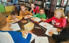 Dzieci siedzą przy stole i kolorują jeżyki.