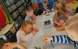 Dzieci siedzą przy białym stole i kolorują jeżyki.