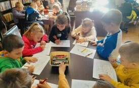 Dzieci siedzą przy stołach i kolorują kolorowanki - jeżyki