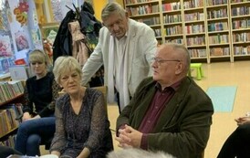 Jeden z czytelnik&oacute;w stoi oparty o krzesła przy kt&oacute;rych siedzą słuchacze i i słucha co m&oacute;wi Pan po prawej stronie.