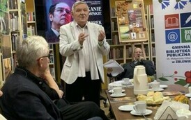 Jeden z czytelnik&oacute;w stoi przy stole i z podniesionymi rękoma o czymś opowiada.