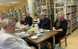 Czytelnicy siedzą przy stołach z kawą i ciastem.