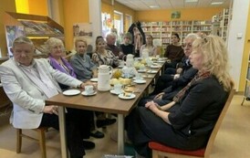 Czytelnicy siedzą przy stołach z kawą i ciastem.