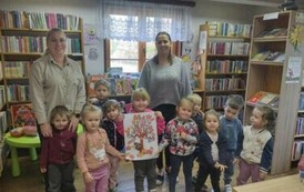 Dzieci stoją w grupie razem ze swoją Panią i Panią z biblioteki. Na środku dziewczynka trzyma kartkę na kt&oacute;rej jest drzewko obklejone listkami.