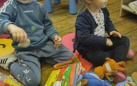 Dzieci siedzą na siedziskach i bawią się pluszowymi książeczkami.