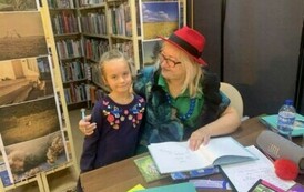 Pani z teatrzyku siedzi przy stoliku i obejmuje ręką dziewczynkę, kt&oacute;ra przyszła dać do podpisu książkę.