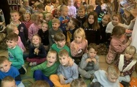 Dzieci gromadnie siedzą na dywanie, a z tyłu stoją aktorzy w przebraniu.