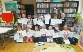 Zdjęcie grupowe dzieci z Panią z biblioteki. Dzieci trzymają w rękach swoje prace plastyczne i się szeroko uśmiechają.