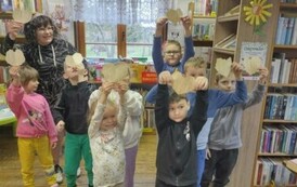 Dzieci stoją razem z Pania pedagog trzymając podniesione wysoko serduszka z papieru od ksiązki.