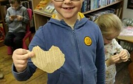 Chłopiec w blond włosach i okularach pokazuje swoje serduszko ze starej kartki od książki.