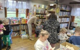 Dzieci stoją w rozsypce, każde dziecko ma starą kartkę od książki i pr&oacute;bują obrywać ją tak aby powstało serduszko. Pani nauczycielka i Pani pedagog pomagają to dzieciom zrobić.