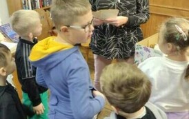 Dzieci stoją przy Pani pedagog, kt&oacute;ra trzyma w rękach stare kartki od książki.