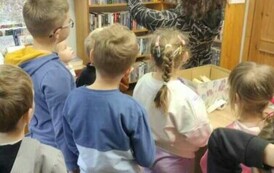 Dzieci stoją przy Pani pedagog, kt&oacute;ra ma podniesione ręce w g&oacute;rze trzymając starą kartkę od książki