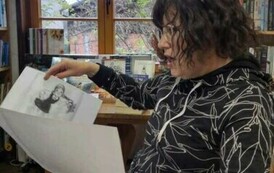 Pani Pedagog patrzy na rozłożoną dużą kartkę z czarnymi ilustracjami, kt&oacute;rą trzyma w rękach.