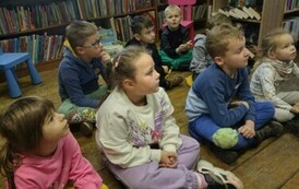 Dzeci siedzą na siedziskach w bibliotece w Borzechowie i słuchają Pani Pedagog.