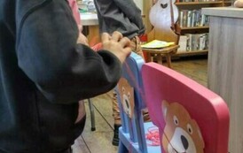 Chłopiec ciągnie włuczkę, kt&oacute;ra jest przymocowana do ust misia, kt&oacute;ry przyklejony jest do oparcia krzesełka wizualizując jedzenie spagetti przez misia.