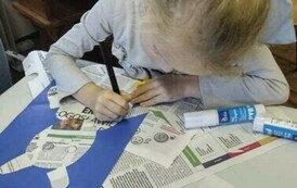 Dziewczynka w blond włosach dekoruje kredką przyklejonego do kartki misia.