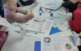 Dzieci przy białym stole wycinają z gazet misie, Pani nauczycielka jest pochylona nas stołem i pomaga.