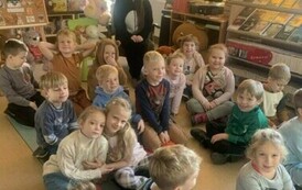 Dzieci siedzą całą grupą na podłodze, a z tyłu siedzi Pani w przebraniu misia.