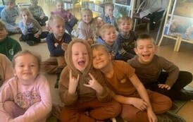 Uśmiechnięte dzieci siedzą na dywanie i słuchają bajki