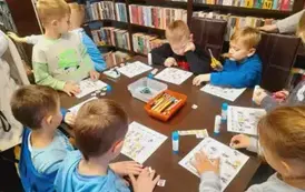 Dzieci siedzą przy stole i uzupełniają obrazkowe sudoku naklejając obrazki w odpowiednie miejsca.