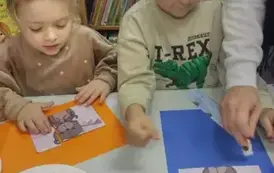 Chłopiec i dziewczynka przy stole naklejają na kolorowe kartki misiowe puzzle, kt&oacute;re leżą na papierowym talerzyku.