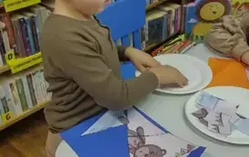 Chłopiec przy stole nakleja misiowe puzzle na niebieską kartkę. Części puzzli leżą na papierowych talerzykach.