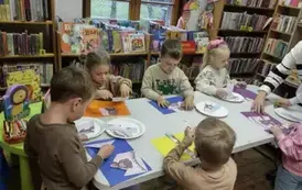 Dzieci siedzą przy stole i naklejają na kolorowe kartki misiowe puzzle.