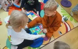 Dzieci na dywanie bawią się pluszowymi książeczkami.