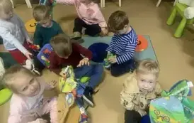 Dzieci siedzą  na siedziskach  w bibliotece i bawią się pluszowymi książeczkami.